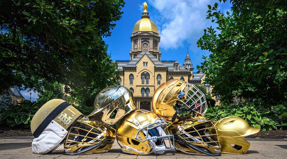 a pile of gold athletic helmets lays on the sidewalk in front of the Golden Dome