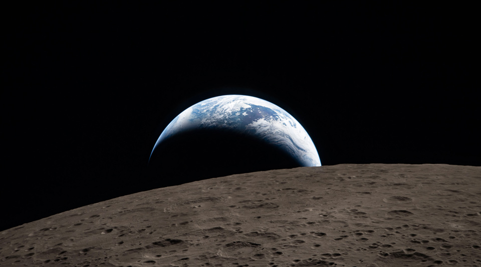 Earthset captured through the Orion spacecraft window during the Artemis II crew’s flyby of the Moon. A muted blue Earth with bright white clouds sets behind the cratered lunar surface.